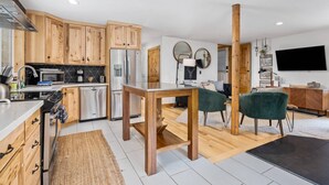 A modern kitchen with wooden cabinets, stainless steel appliances, and a dining area with a wooden table and two chairs.