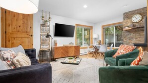 A modern living room with a fireplace, a TV, and a dining area with a view of the outdoors.