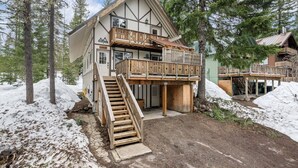 A chalet with a wooden staircase leading to a balcony, surrounded by snow and trees.