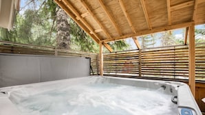 A hot tub under a wooden pergola with a view of trees.