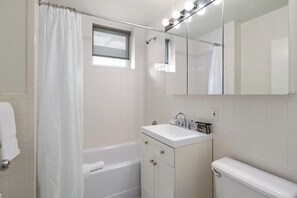 A bathroom with a bathtub, a sink, a toilet, a mirror, and a window.