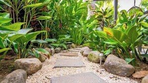 Un sentiero nel giardino con pietre di mosaico e rocce, circondato da piante verdi e rigogliose.