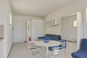 Ein moderner, gut beleuchteter Raum mit einem runden Esstisch, Stühlen, einem blauen Sofa und einem weißen Kleiderschrank.