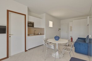 Une cuisine moderne avec des meubles blancs, une table de salle à manger ronde entourée de chaises en métal, et un bol bleu posé sur la table.