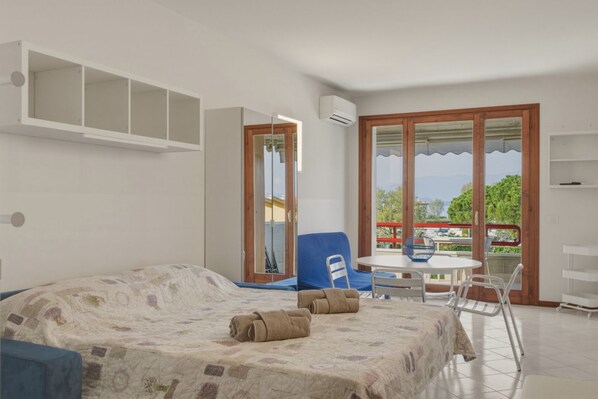 Ein Schlafzimmer mit Bett, Stuhl, Tisch und einem Balkon mit Aussicht.