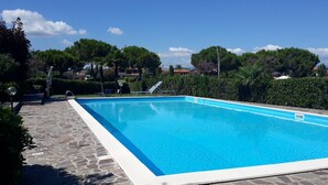 Una piscina rectangular con agua azul cristalina, rodeada de baldosas de piedra y abundante vegetación.