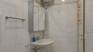 Un baño con baldosas de mármol blanco, un lavabo blanco, un espejo y un perchero para toallas.