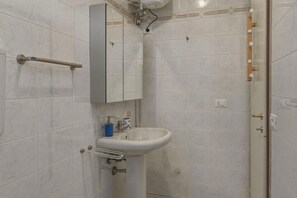 A bathroom with white marble tiles, a white sink, a mirror, and a towel rack.