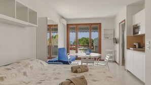 Un dormitorio con cama, una mesa de comedor con sillas, una zona de cocina y vistas a través de una ventana.