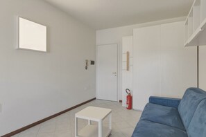 Ein Zimmer mit einem blauen Sofa, einem weißen Tisch, einer weißen Tür und einem Feuerlöscher.