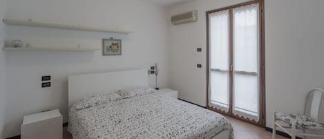 A bedroom with a bed, a nightstand, a chair, a window with blinds, and a ceiling light.
