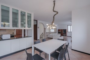 A modern kitchen with white cabinets, a dining table with chairs, and a unique twisted ceiling light fixture.