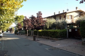 A residential street with a house featuring a balcony, a satellite dish, and a gated entrance.