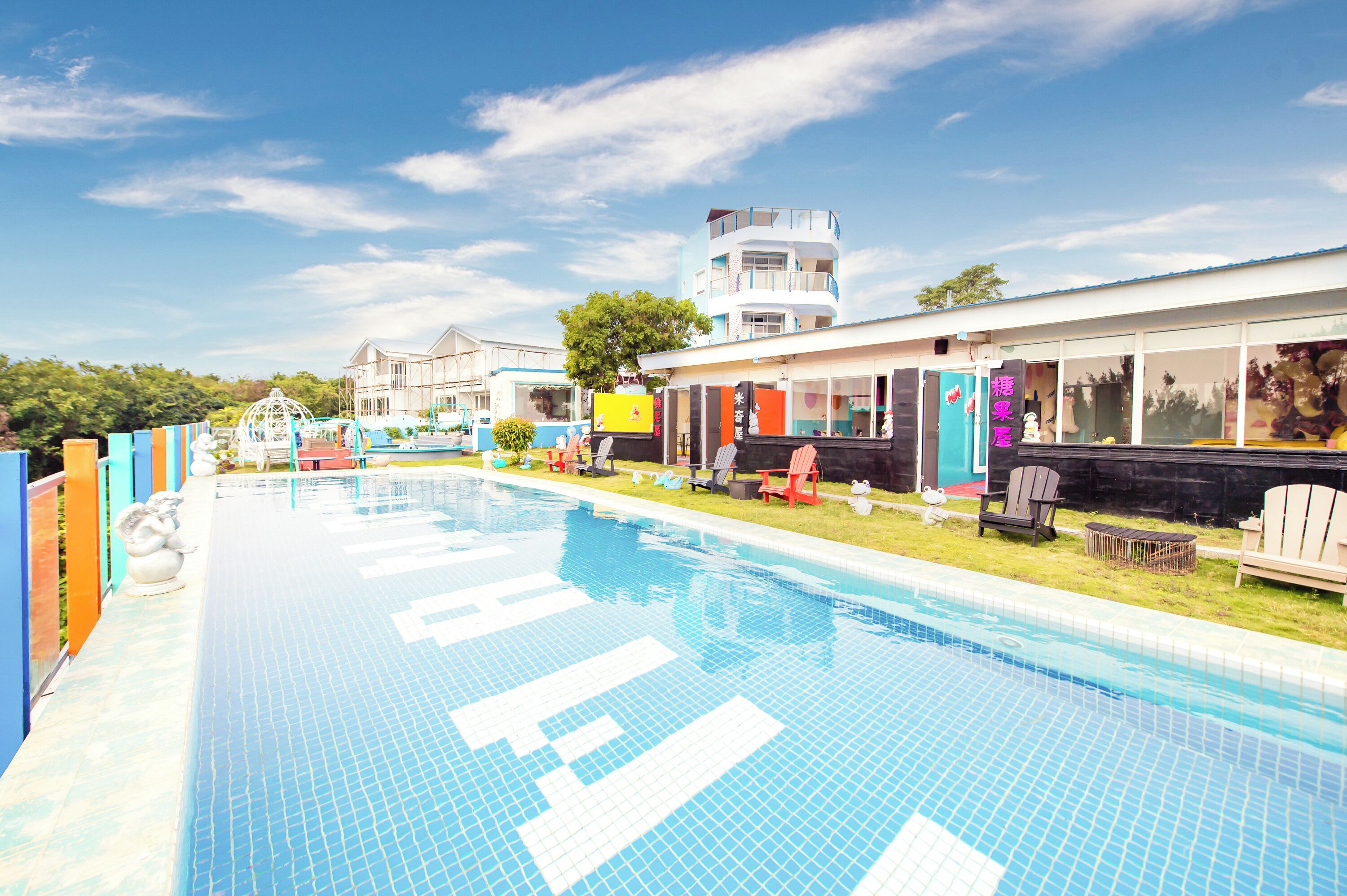 Una piscina con solarium empedrado, rodeada de mobiliario exterior y un edificio de varios pisos.