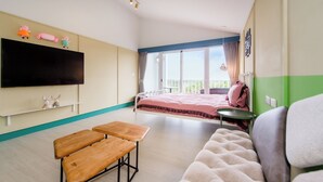 A room with a bed, a TV, two wooden benches, a sofa, and a balcony with a view. - Happiness Pink B&B (Liuqiu)