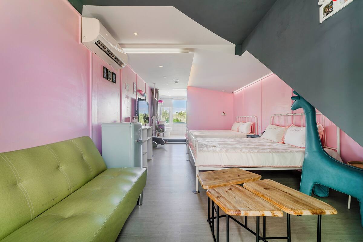 A modern hotel room with a green sofa, a wooden bench, a bed with a white mattress, and a teal chair.