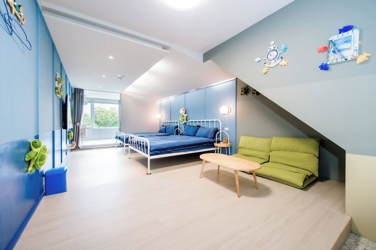A modern bedroom with a bed, a green sofa, a small table, and a large window.