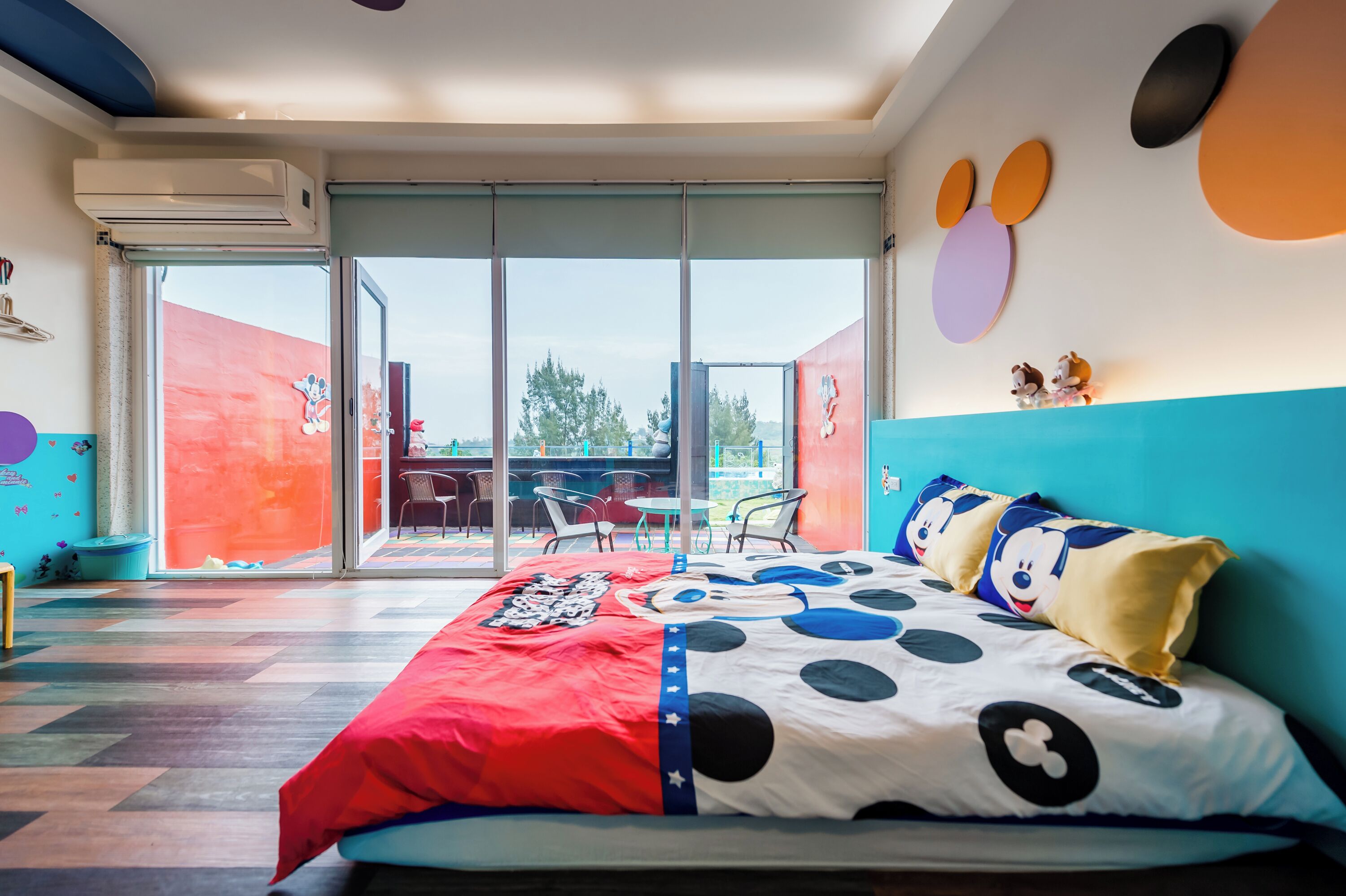 A modern bedroom with a large bed, a sliding glass door to a balcony, and colorful wall decorations.