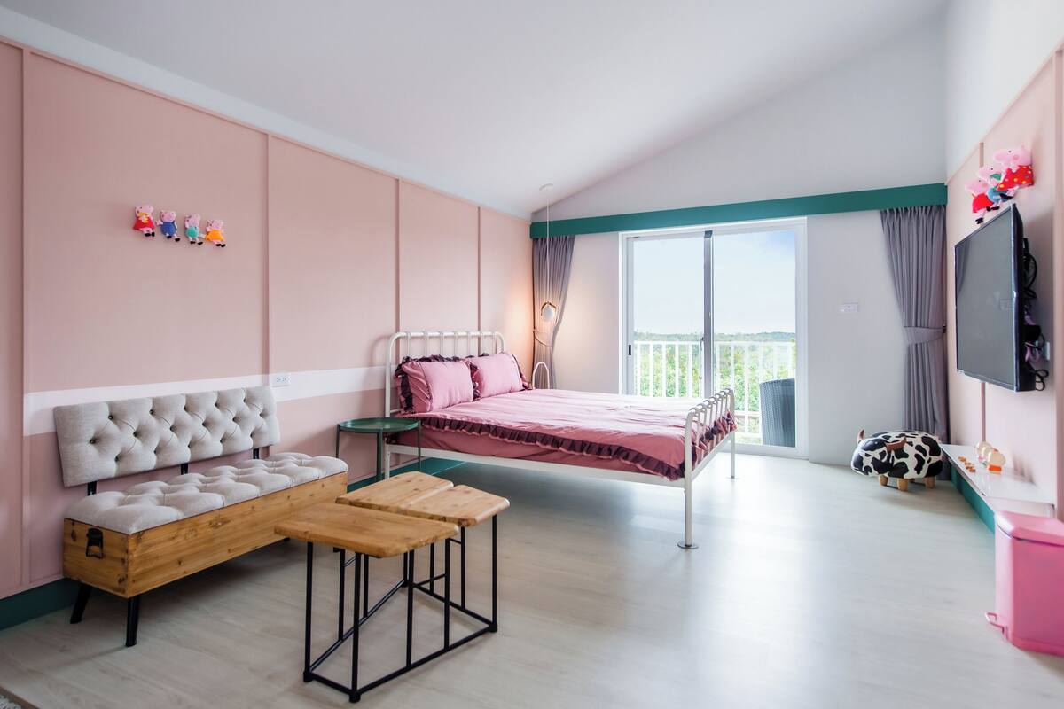 A bedroom with a bed, a sofa, a small table, a TV, and a balcony with a view.