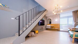 A modern living room with a staircase, a sofa set, a kitchen area, and a large window offering a view. - Happiness Pink B&B (Liuqiu)