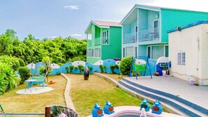 A swimming pool with a fountain, surrounded by a blue fence, and a two-story building with balconies. - Happiness Pink B&B (Liuqiu)