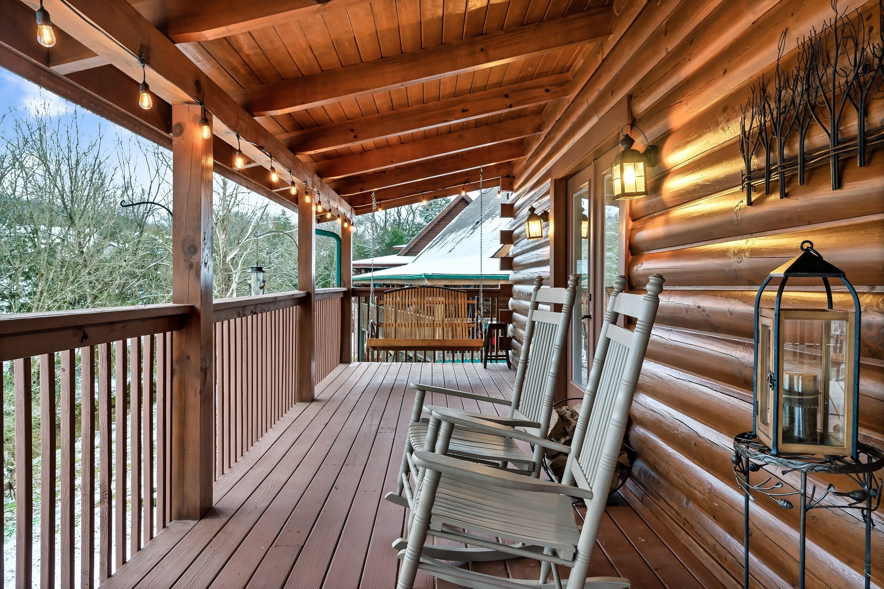 A wooden deck with rocking chairs and a lantern, overlooking a green landscape.