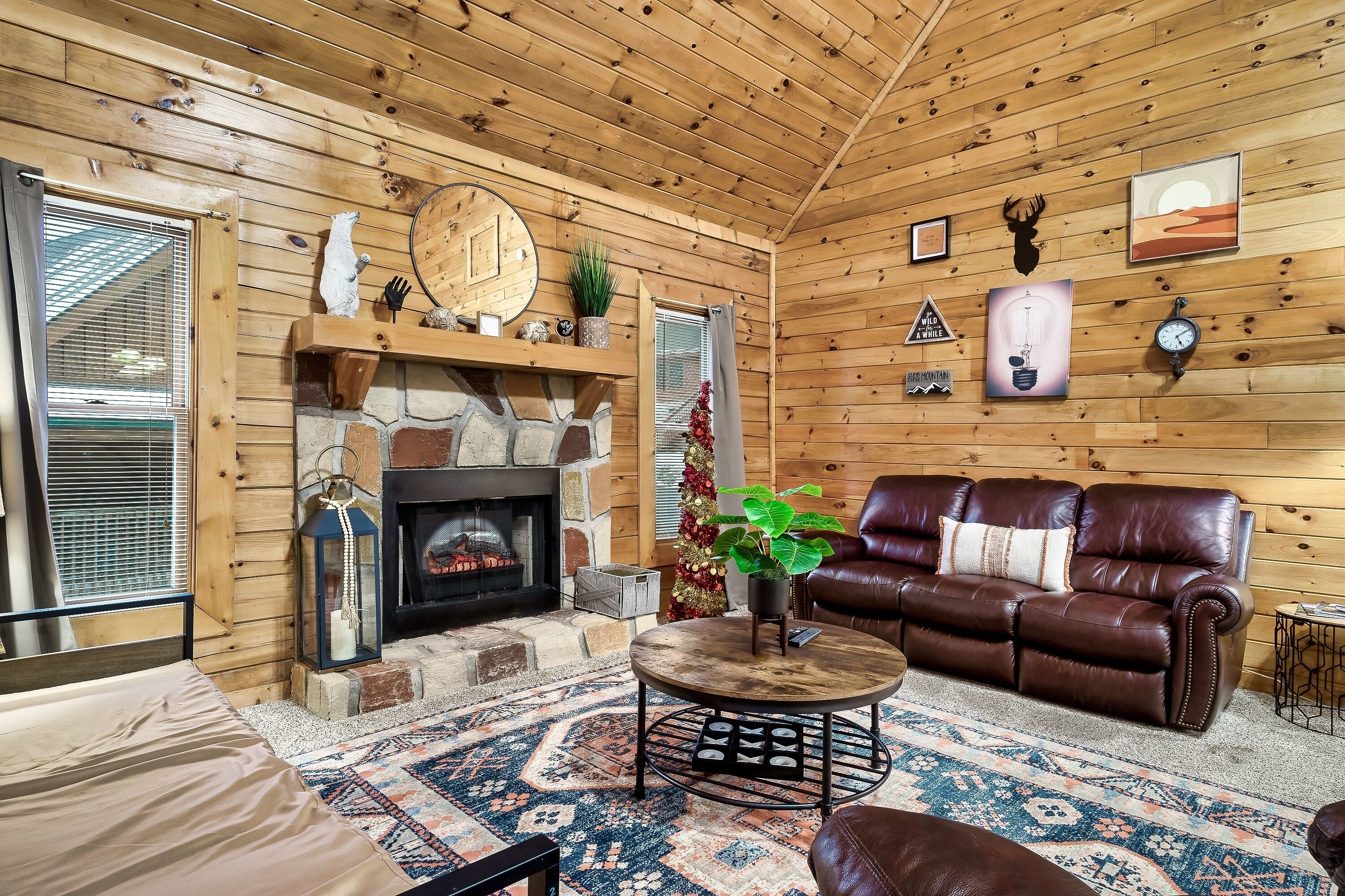 A cozy log cabin interior with a fireplace, leather sofa, and a patterned rug.