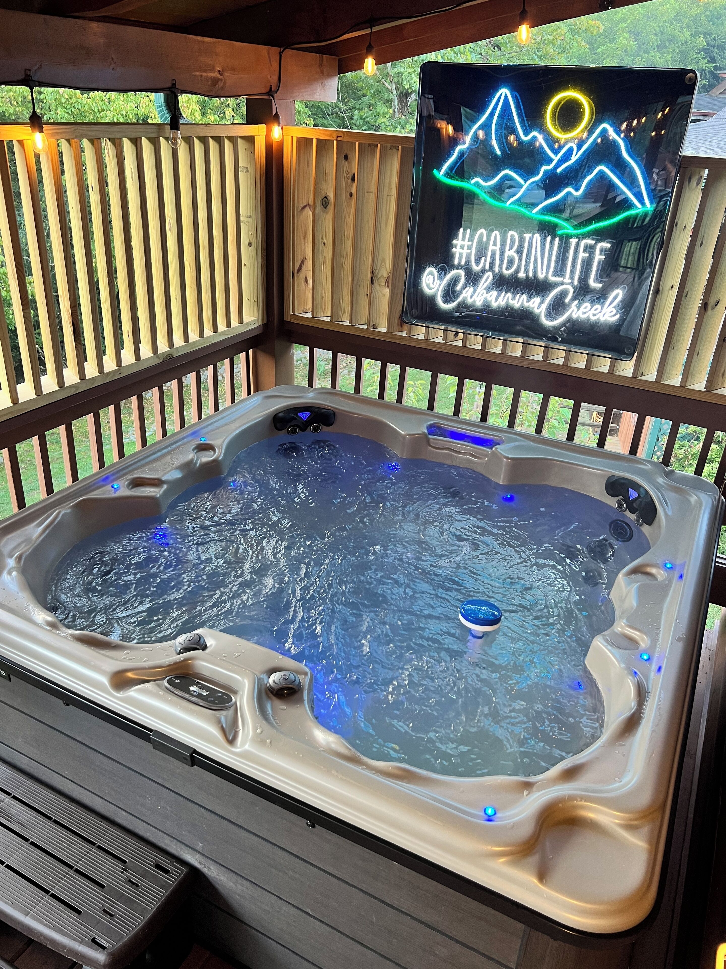 A hot tub with a wooden deck and a neon sign above it.