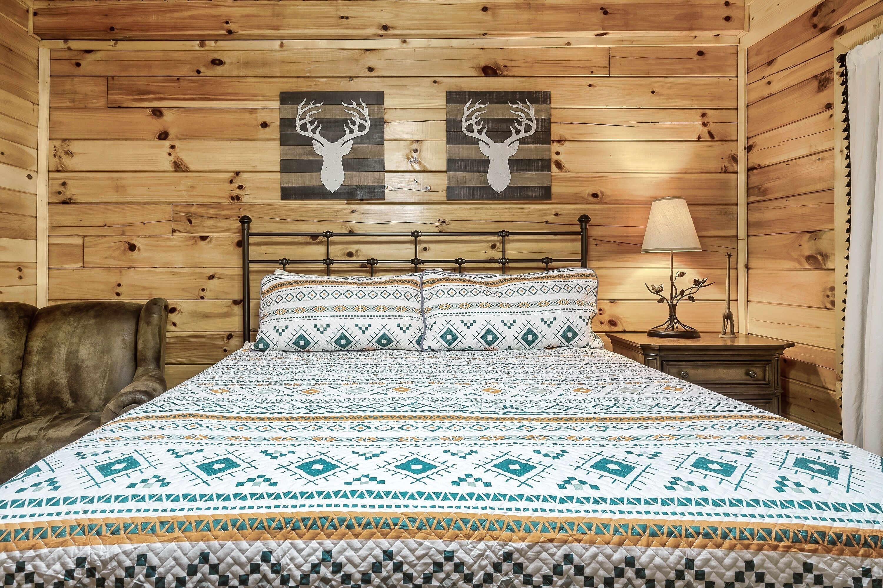 Une chambre à coucher de style cabane en bois, avec un lit, deux têtes de cerf décoratives au mur, une lampe et une chaise.
