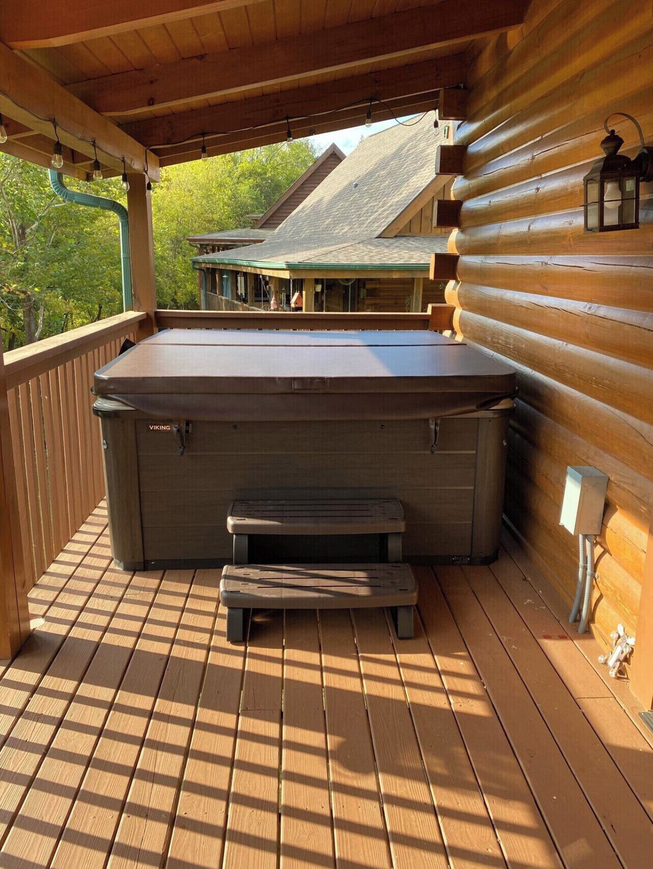 A wooden deck with a hot tub and a bench, overlooking a cabin with a green roof.