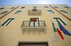 Un edificio con varios balcones, algunos con plantas. Hay banderas a la derecha.