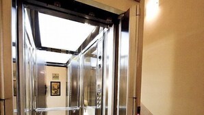 Ein Aufzug mit Glastür, Metallrahmen und einer Leuchte darüber.