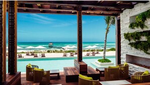 Eine Holzterrasse mit Sitzgelegenheiten, mit Blick auf einen Pool und einen Strand.