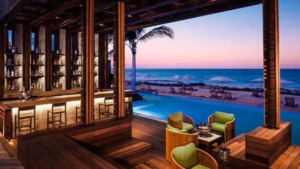 Eine Holzbar mit Sitzgelegenheiten am Pool mit Blick auf einen Strand bei Sonnenuntergang.
