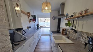 Ett modernt kök med en lång arbetsbänk, en inbyggd ugn och en stor diskho. Det finns en hängande lampa och ett fönster som släpper in naturligt ljus.