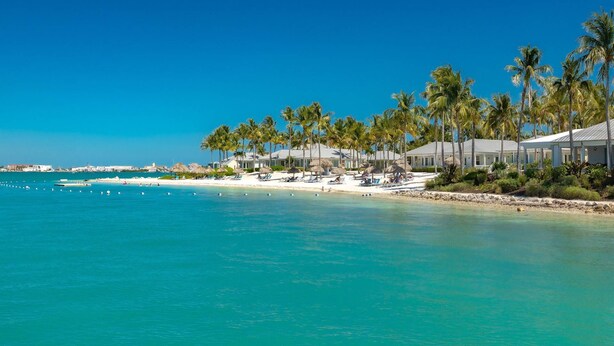 A beach resort with white buildings, palm trees, and clear blue water. - Luxury Sunset Key Cottage | Beach, Pool & Latitudes | 30+ Night Rental (Key West)