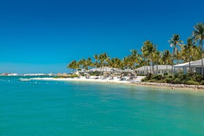 A beach resort with white buildings, palm trees, and clear blue water. - Luxury Sunset Key Cottage | Beach, Pool & Latitudes | 30+ Night Rental (Key West)