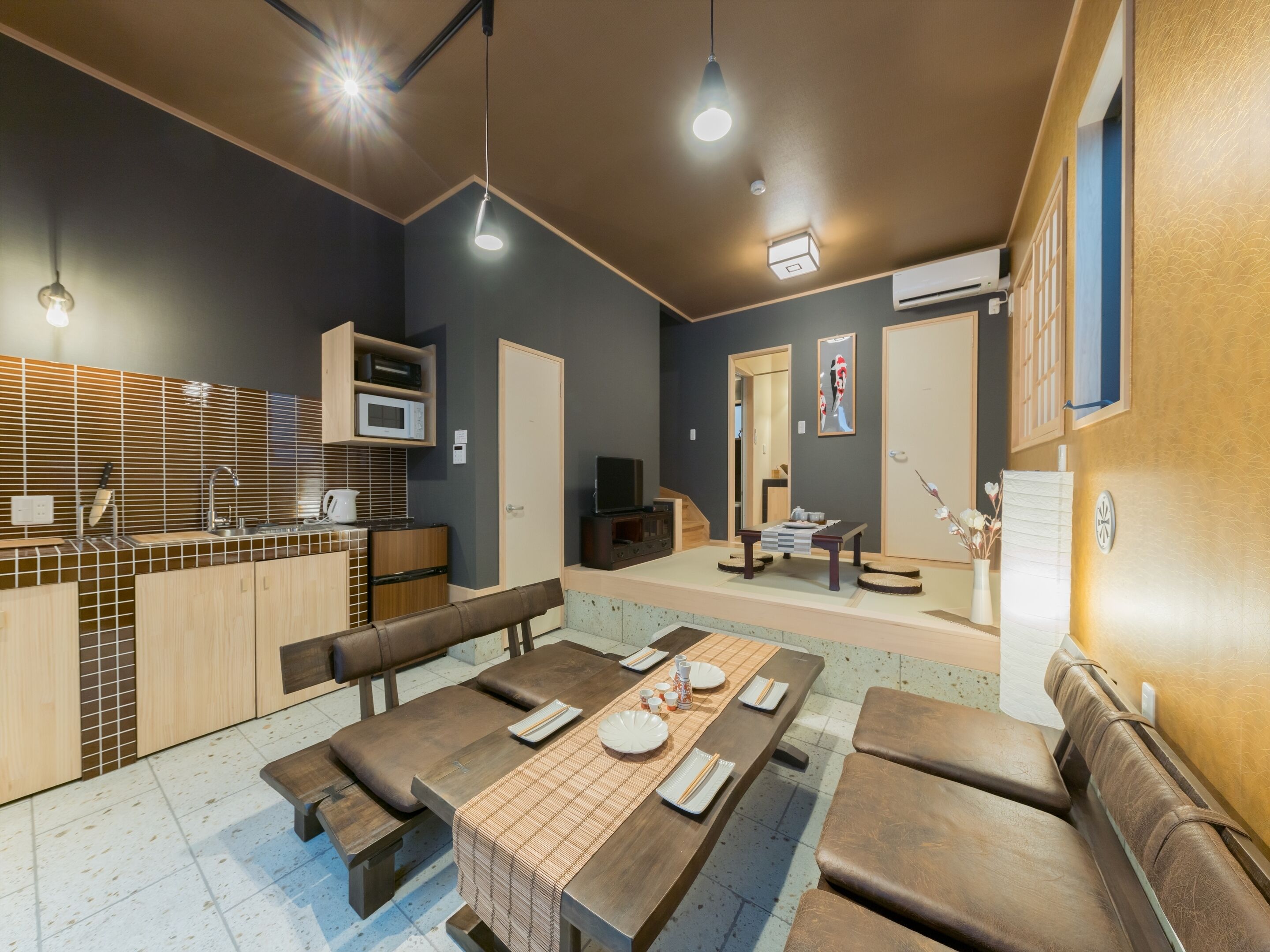 Una cocina moderna con microondas, pileta y muebles de madera. Cuenta con un comedor con mesa y bancos, y un pequeño espacio de estar con sofá.