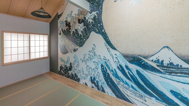 Une pièce avec un sol recouvert de tatamis et un tableau représentant une vague, dans le style traditionnel japonais, accroché au mur.