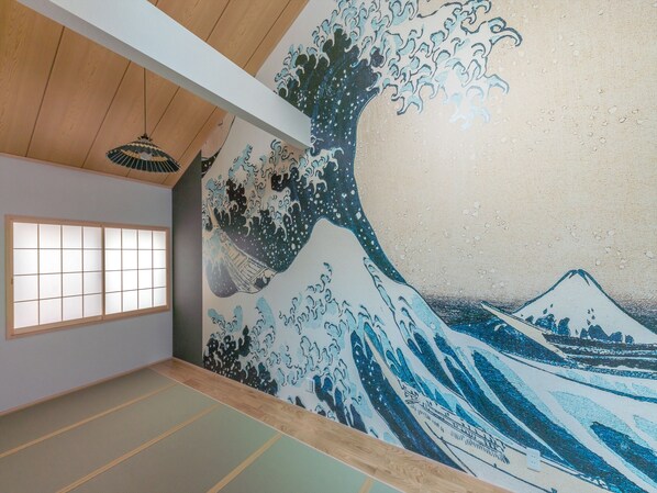 Une pièce avec un sol recouvert de tatamis et un tableau représentant une vague, dans le style traditionnel japonais, accroché au mur.