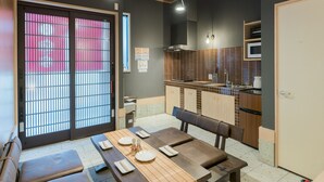 Une cuisine moderne équipée d’un four à micro-ondes, d’un évier et de meubles en bois. On y trouve un coin repas avec une table dressée pour deux personnes, un banc et une vue sur un bâtiment rouge à l’extérieur.