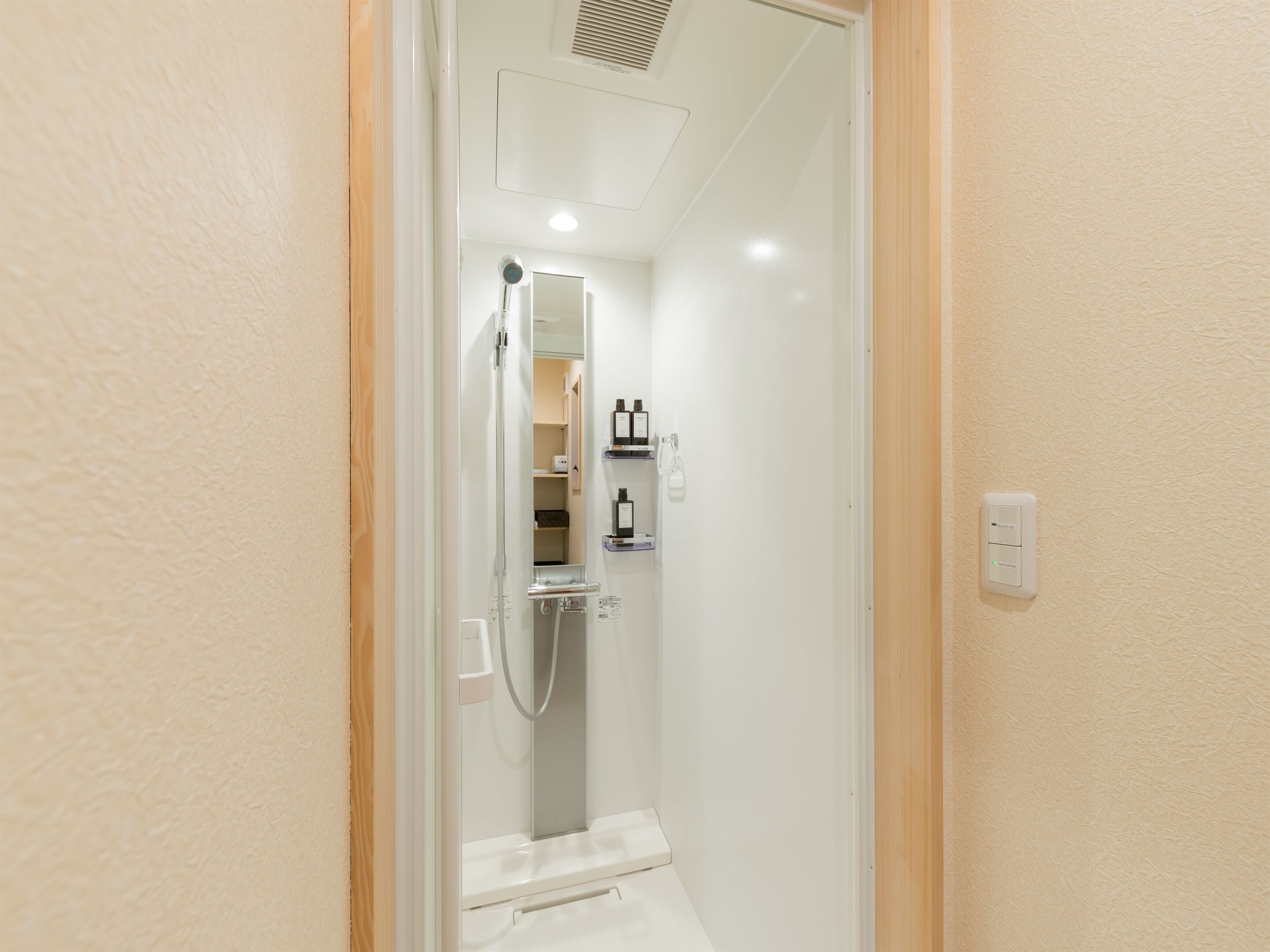 Un baño estrecho y bien iluminado con ducha, espejo y repisa con artículos de aseo.