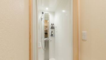 Un baño estrecho y bien iluminado con ducha, espejo y repisa con artículos de aseo.