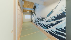 Un couloir avec des tatamis au sol, un paravent de style shoji et un tableau représentant une vague accroché au mur.