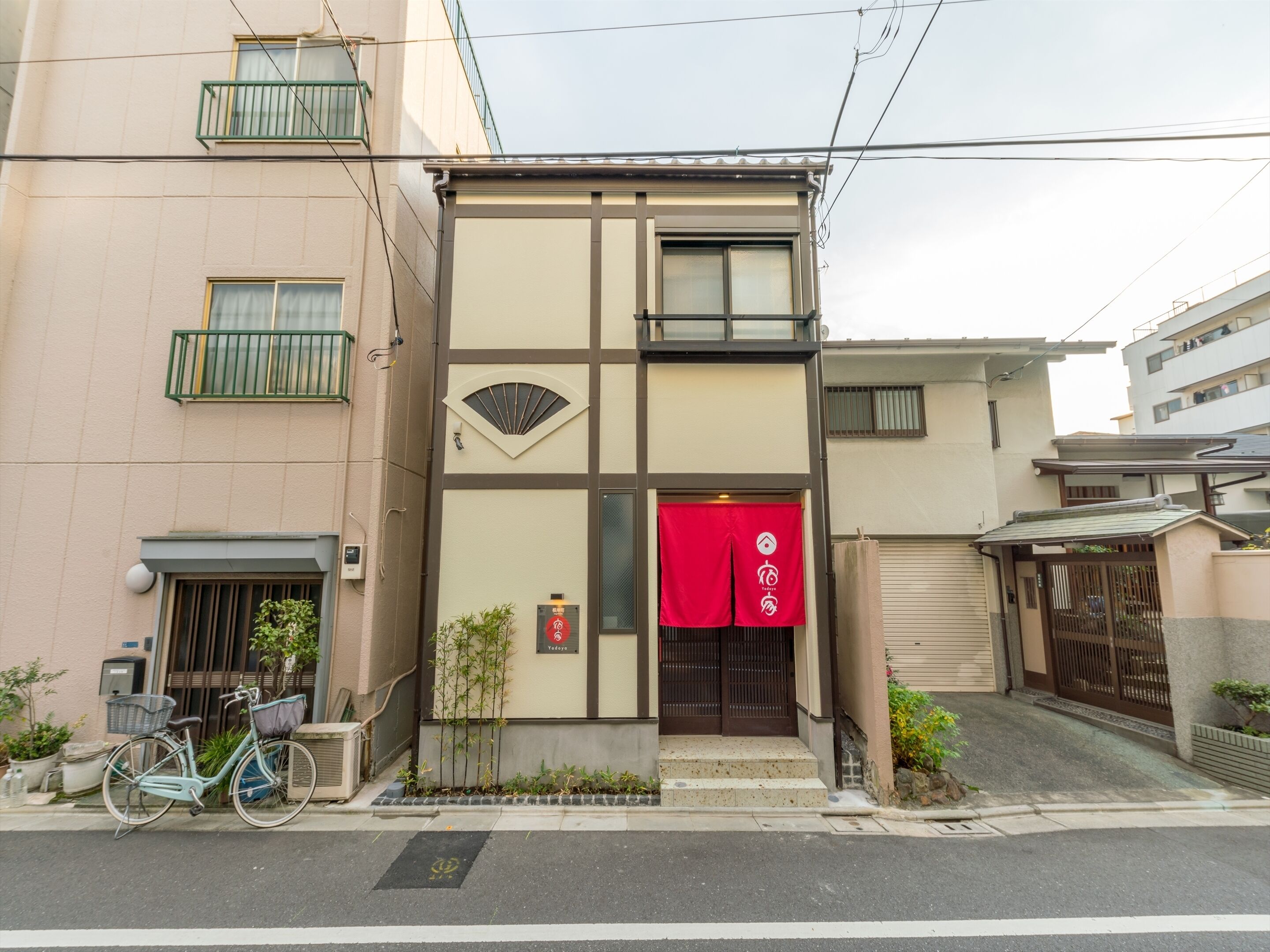 A building with a traditional Japanese entrance, a bicycle parked outside, and a small tree in front.