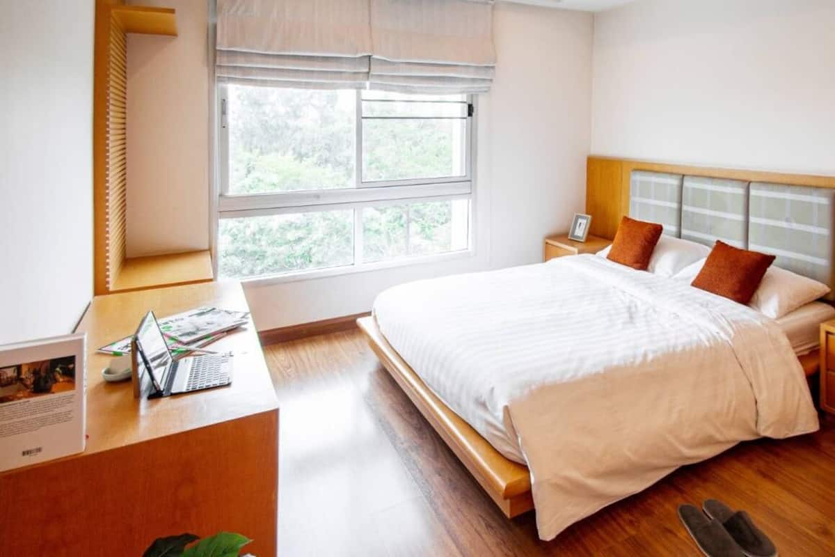 A bedroom with a bed, bedside tables, a desk with a laptop, and a window with blinds.