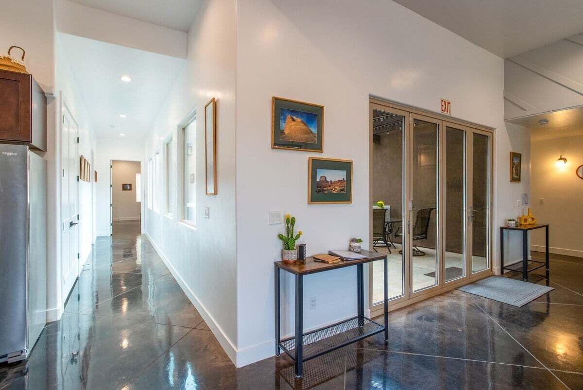 A hallway with a polished floor, a sliding glass door leading to a room, and framed pictures on the wall.