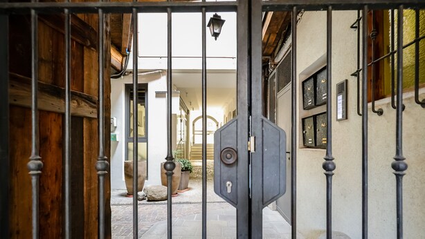 Un patio amurallado con suelo de piedra, plantas en macetas y una puerta de metal.