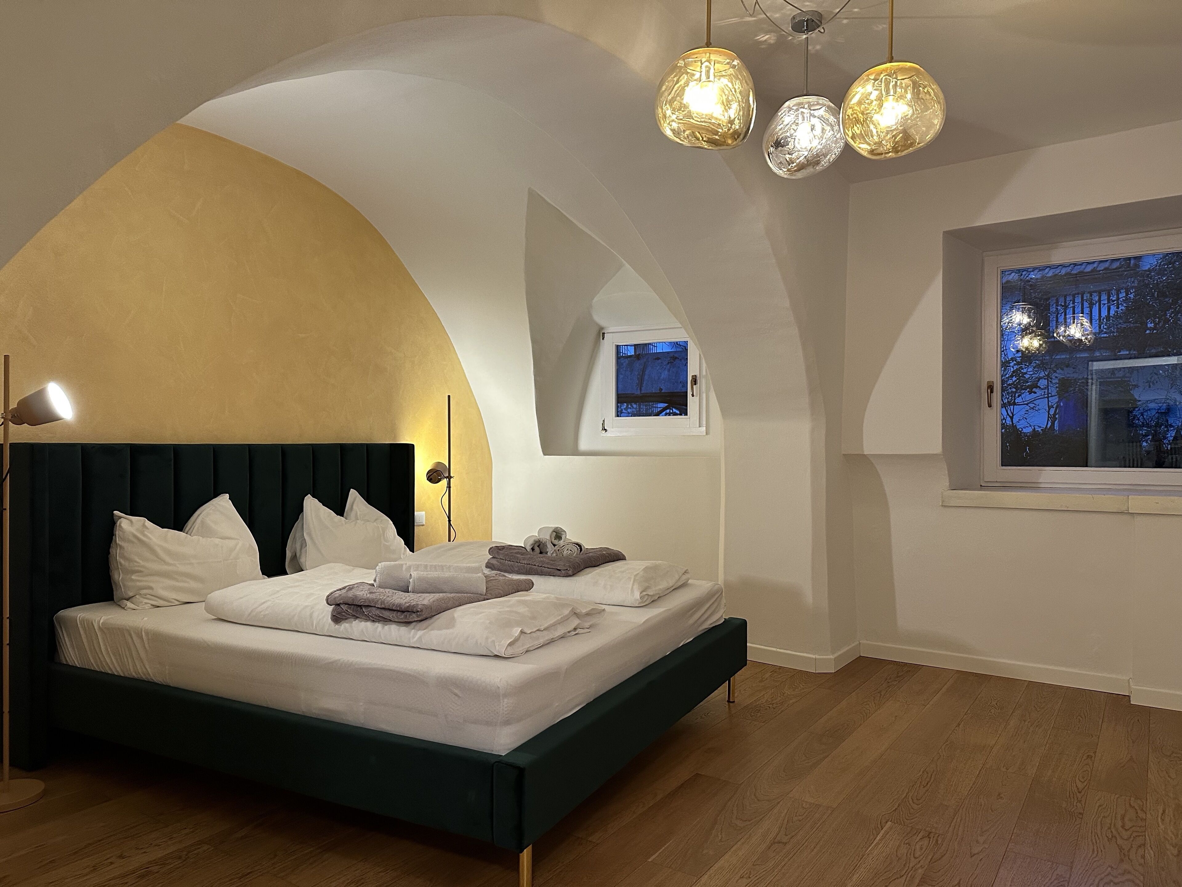 A bedroom with a bed, a bedside lamp, a window, and a ceiling light fixture.