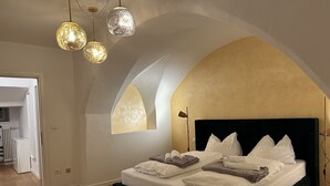Un dormitorio con techo abovedado, cama con ropa blanca y varios almohadones, una lámpara de pie y un aplique en el techo.